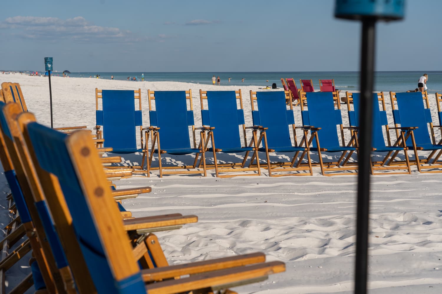 Blue and red beach chairs lined up in rows on the white sand with the ocean in the background