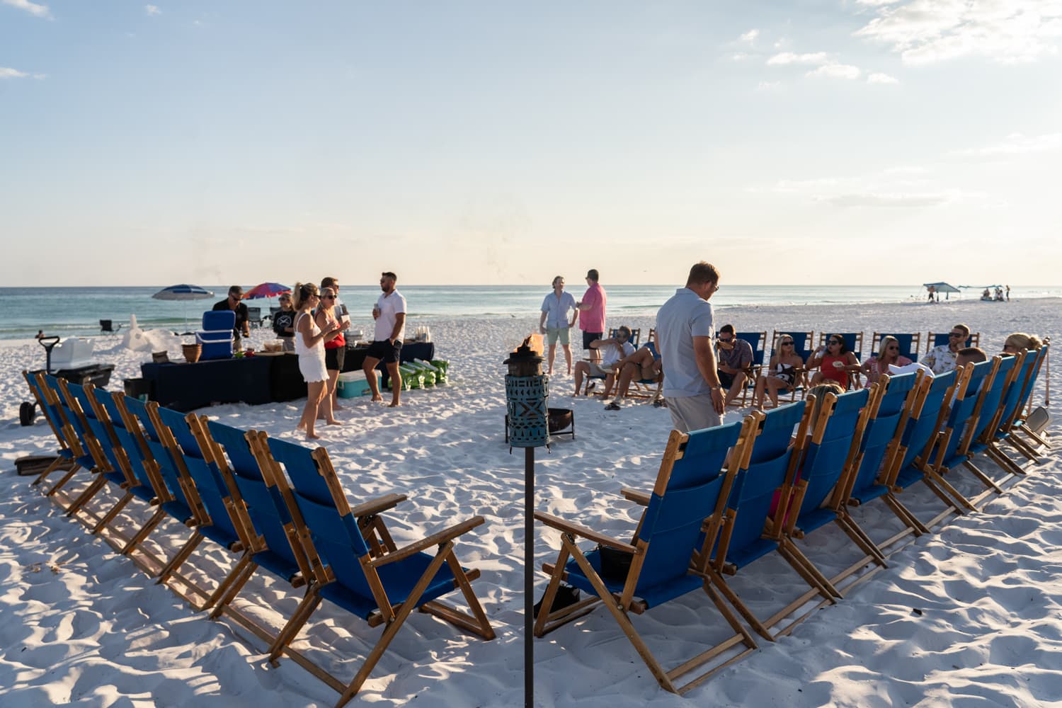 Guests gathering for a beach bonfire event with chairs circled around the fire pit as the sun sets over the Gulf